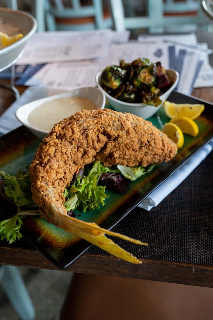 Delicious crispy fried fish served with lemon wedges and fresh greens for a tasty meal.